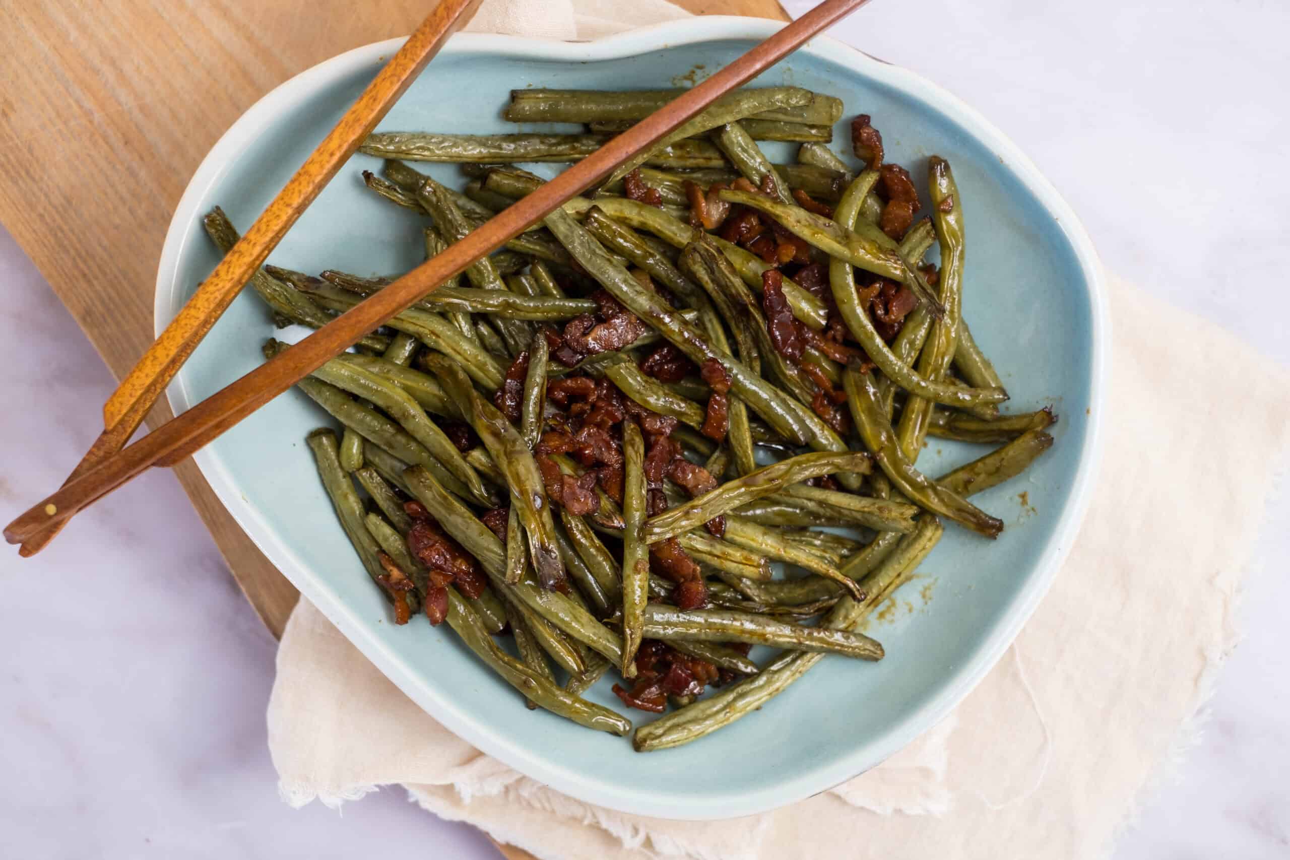 Green beans with bacon, cooked to perfection, on a light blue plate, garnished with crispy bacon pieces. A delicious and savory vegetable dish perfect for side meals or family dinners.