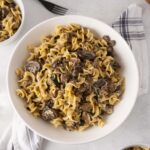 Creamy mushroom and ground beef pasta served on a white plate with side bowls, ideal for comfort food recipes and quick weeknight dinners.
