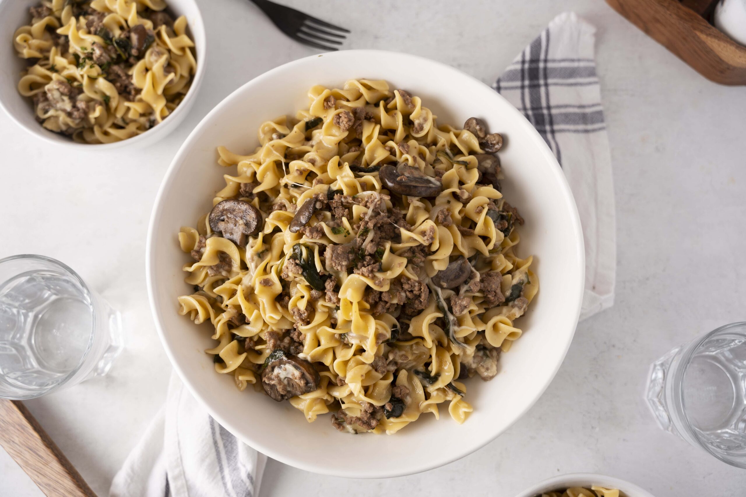 Creamy mushroom and ground beef pasta served on a white plate with side bowls, ideal for comfort food recipes and quick weeknight dinners.
