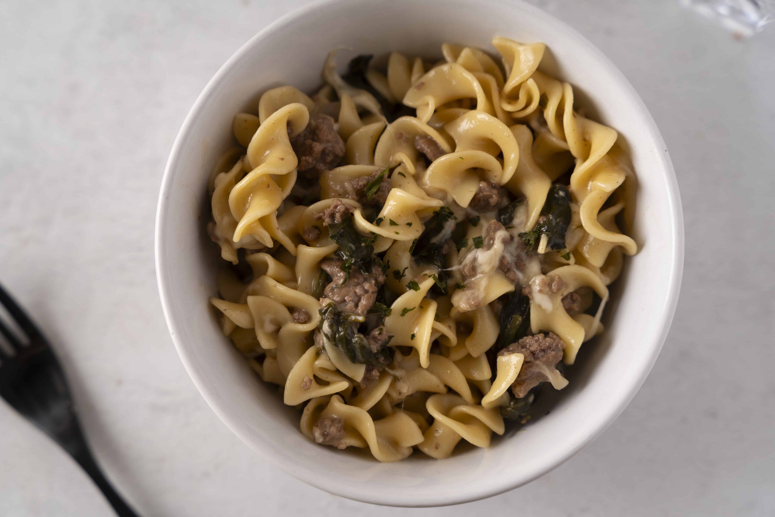 Creamy beef and spinach tortellini in a rich sauce served in a white bowl, perfect for a comforting meal.