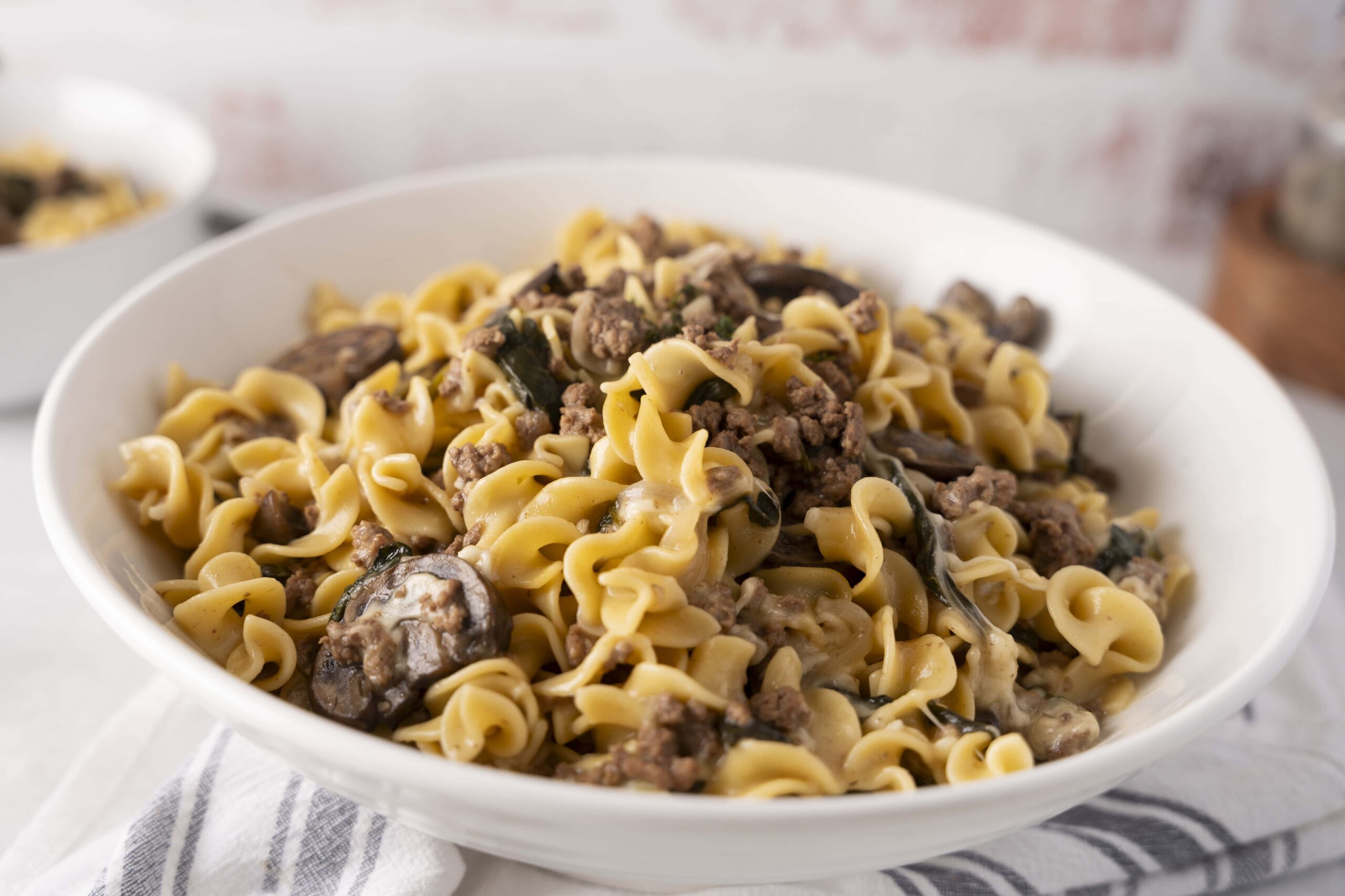 Creamy beef stroganoff with egg noodles, mushrooms, and herbs in a white bowl, served on a rustic table.