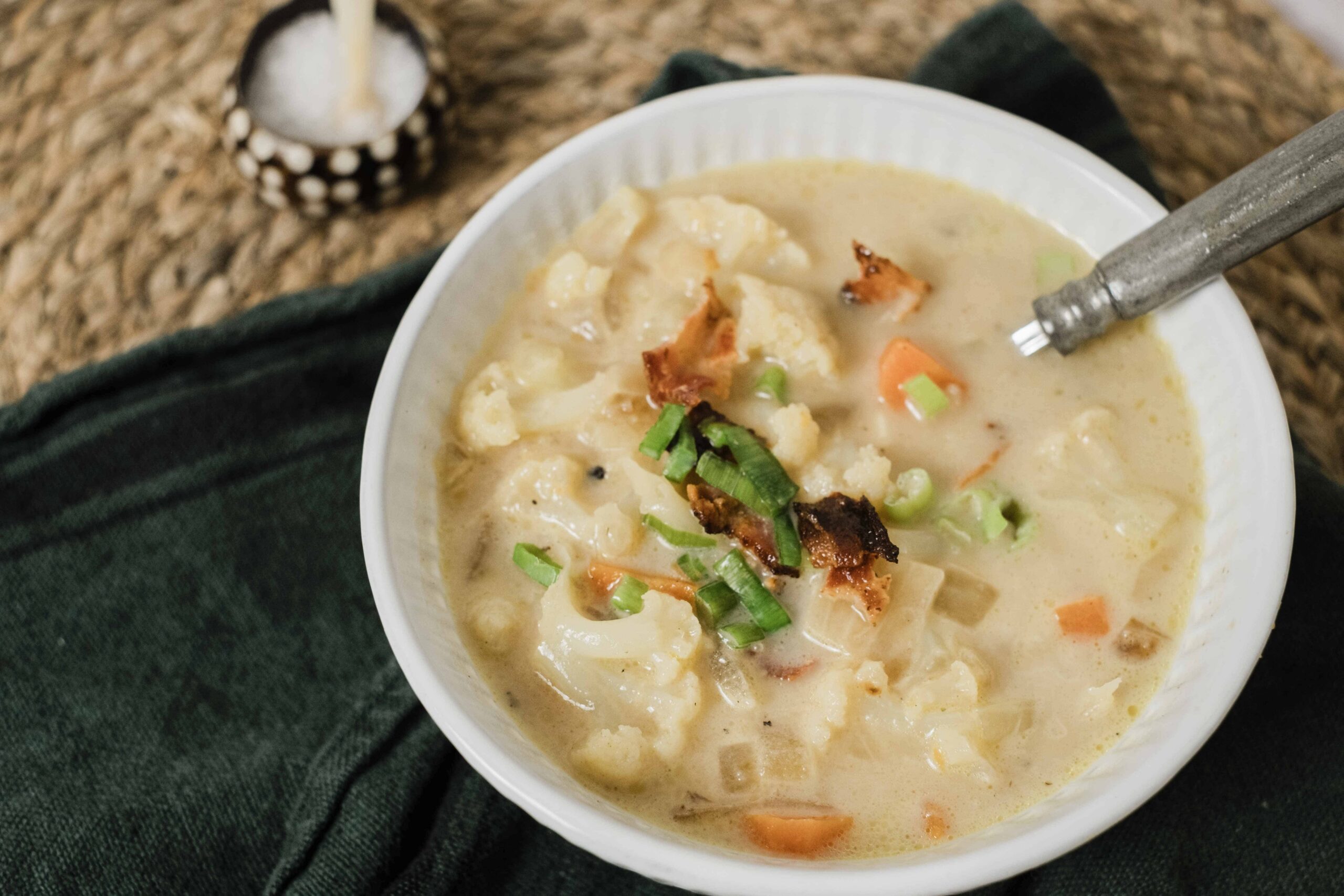 Creamy vegetable chicken pot pie soup with cauliflower, carrots, green onions, topped with crispy bacon bits and fresh herbs, served in a white bowl for a hearty homemade meal.