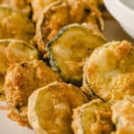 Crispy baked zucchini fries with golden breadcrumb coating, served on a white plate with a dipping sauce, ideal for a healthy snack or side dish.