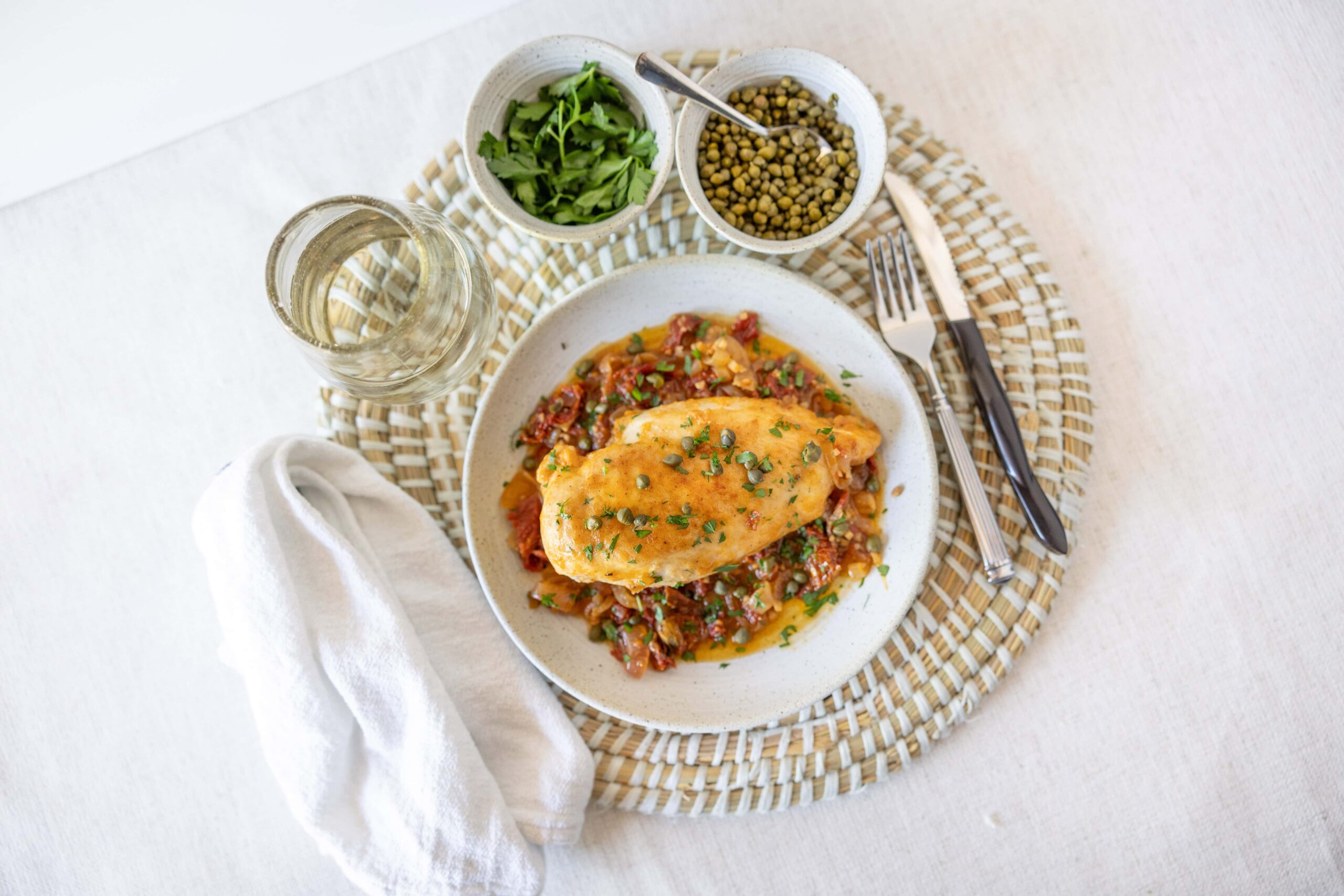 Juicy baked chicken breast served over vegetable medley with herbs, alongside fresh greens and lentils on a white plate, perfect for healthy meal ideas.