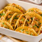 Savory beef and chicken tacos with melted cheese, fresh cilantro, and flavorful toppings in a white serving dish. Perfect for a delicious Mexican meal.