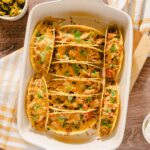 Creamy baked beef taco casserole topped with melted cheese and fresh cilantro, served in a white dish with sour cream, cheese, and toppings on a rustic wooden table.