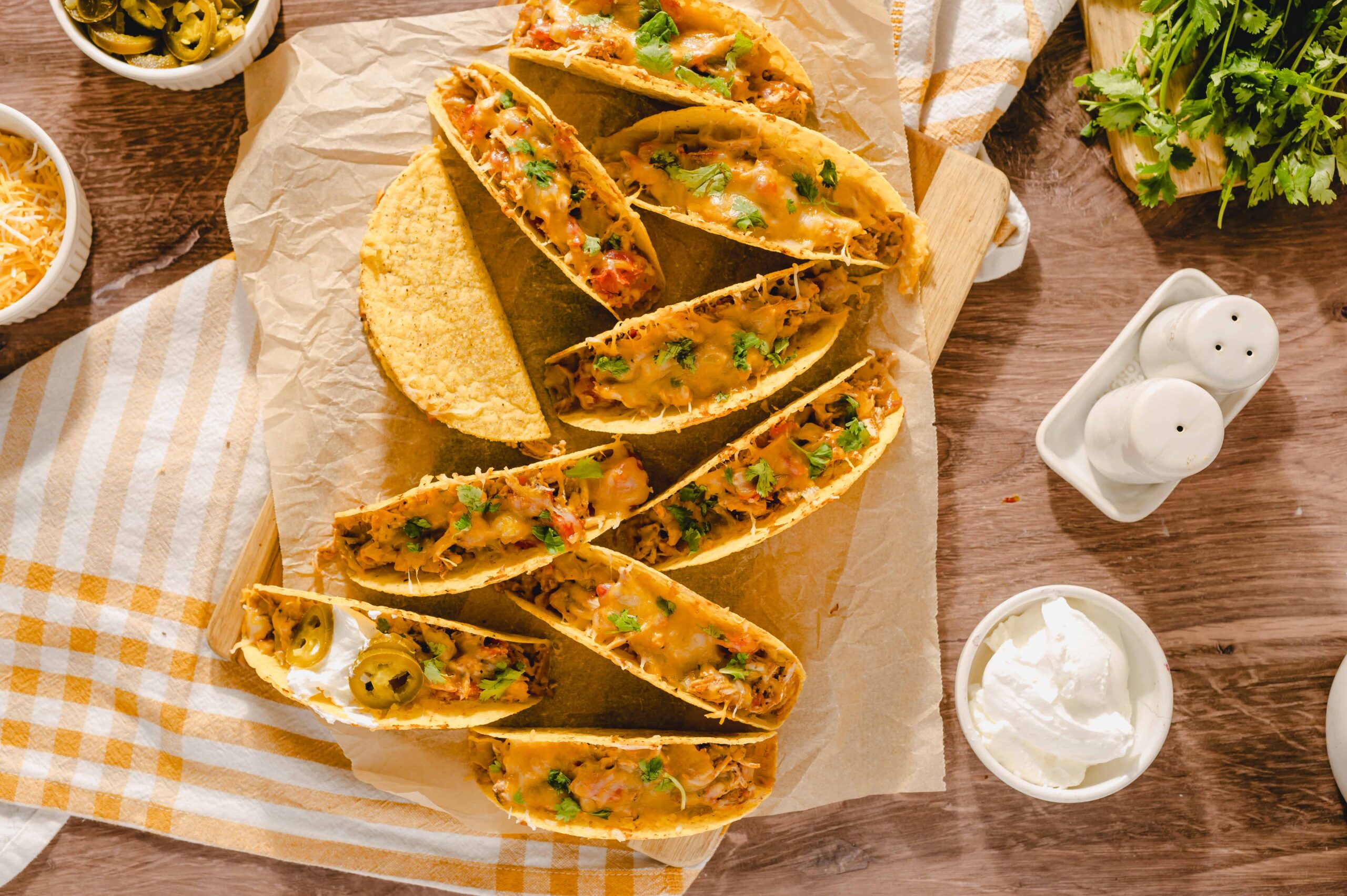 Savory crunchy tacos filled with seasoned meat, cheese, and fresh herbs on a wooden serving board with toppings and condiments around, perfect for Mexican cuisine lovers.