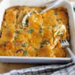 Creamy baked buffalo chicken casserole topped with melted cheese and fresh cilantro, served in a white baking dish with a side of green dip, perfect for comfort food lovers and family dinners.