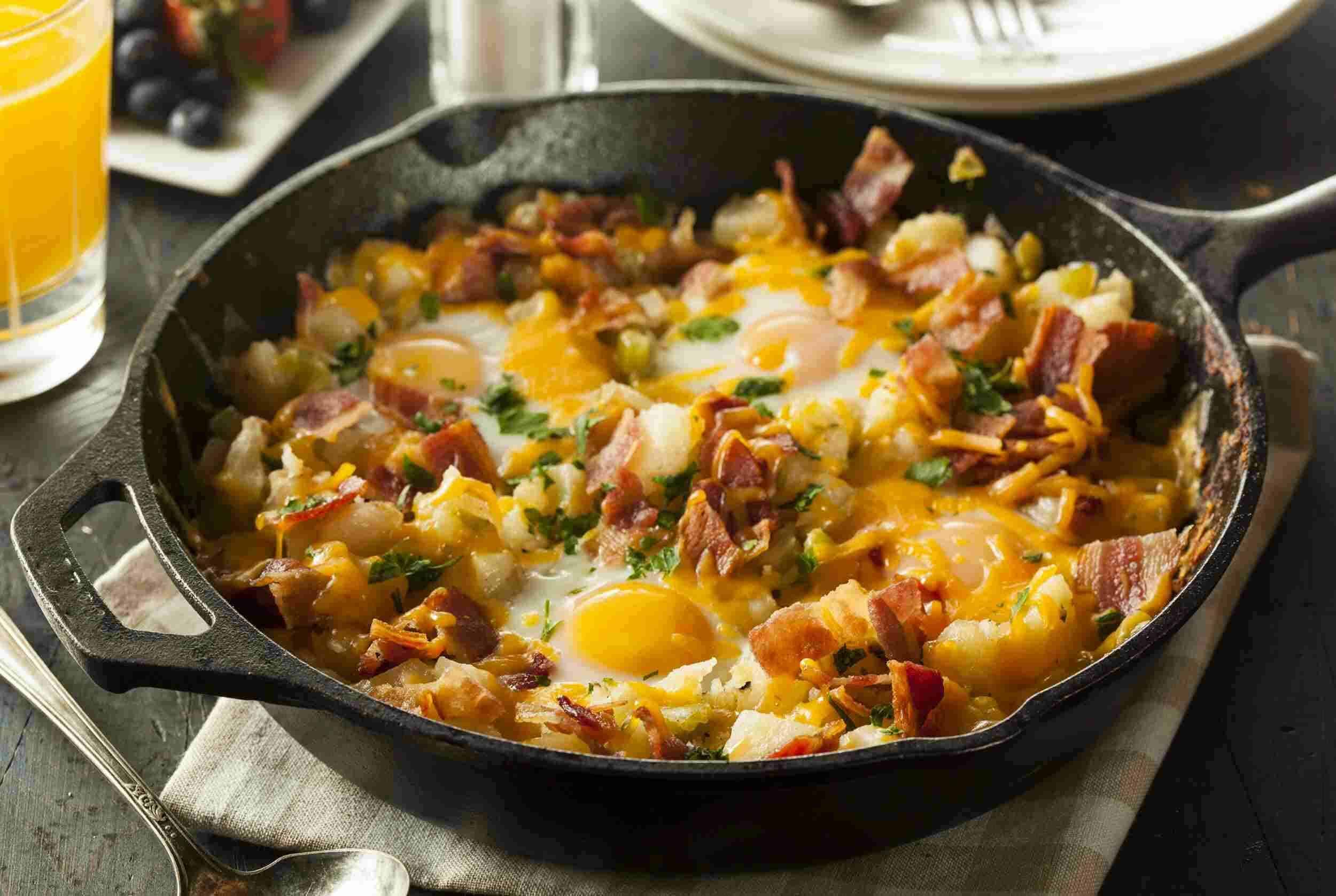 Crispy bacon and cheddar egg skillet with potatoes and green onions, served in a black cast iron pan for breakfast or brunch, featuring savory and cheesy flavors.