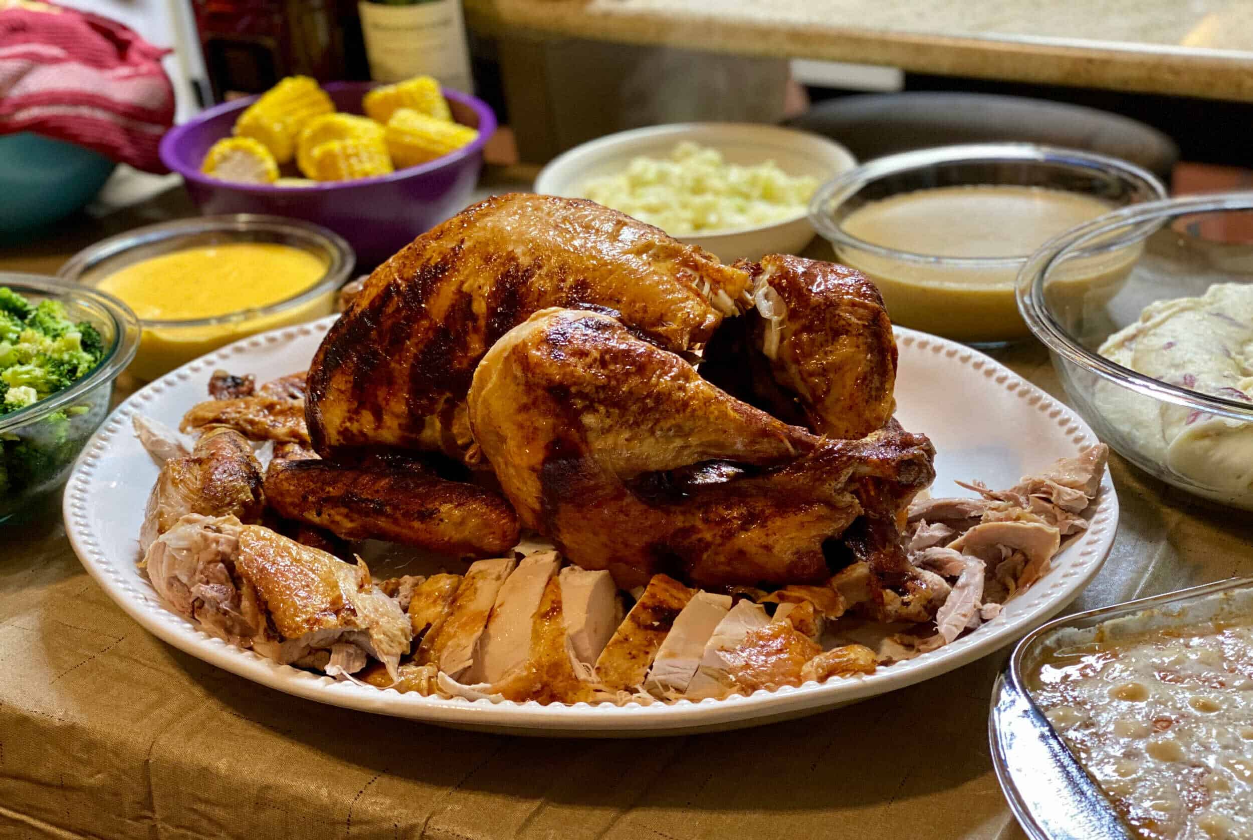 Roast whole chicken with sliced meat, surrounded by various side dishes and sauces on a festive dining table.