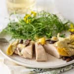 Succulent poached chicken breast topped with artichoke hearts and mushrooms, served with fresh greens and edible flowers on a white plate for a elegant and healthy meal.