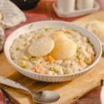 Creamy chicken and vegetable pot pie filling with dumplings served in a white bowl - comfort food recipe.