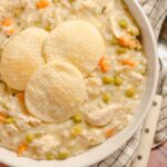Creamy chicken and vegetable pot pie with peas, carrots, and flaky cornbread on top, served in a white bowl for a comforting homemade meal.