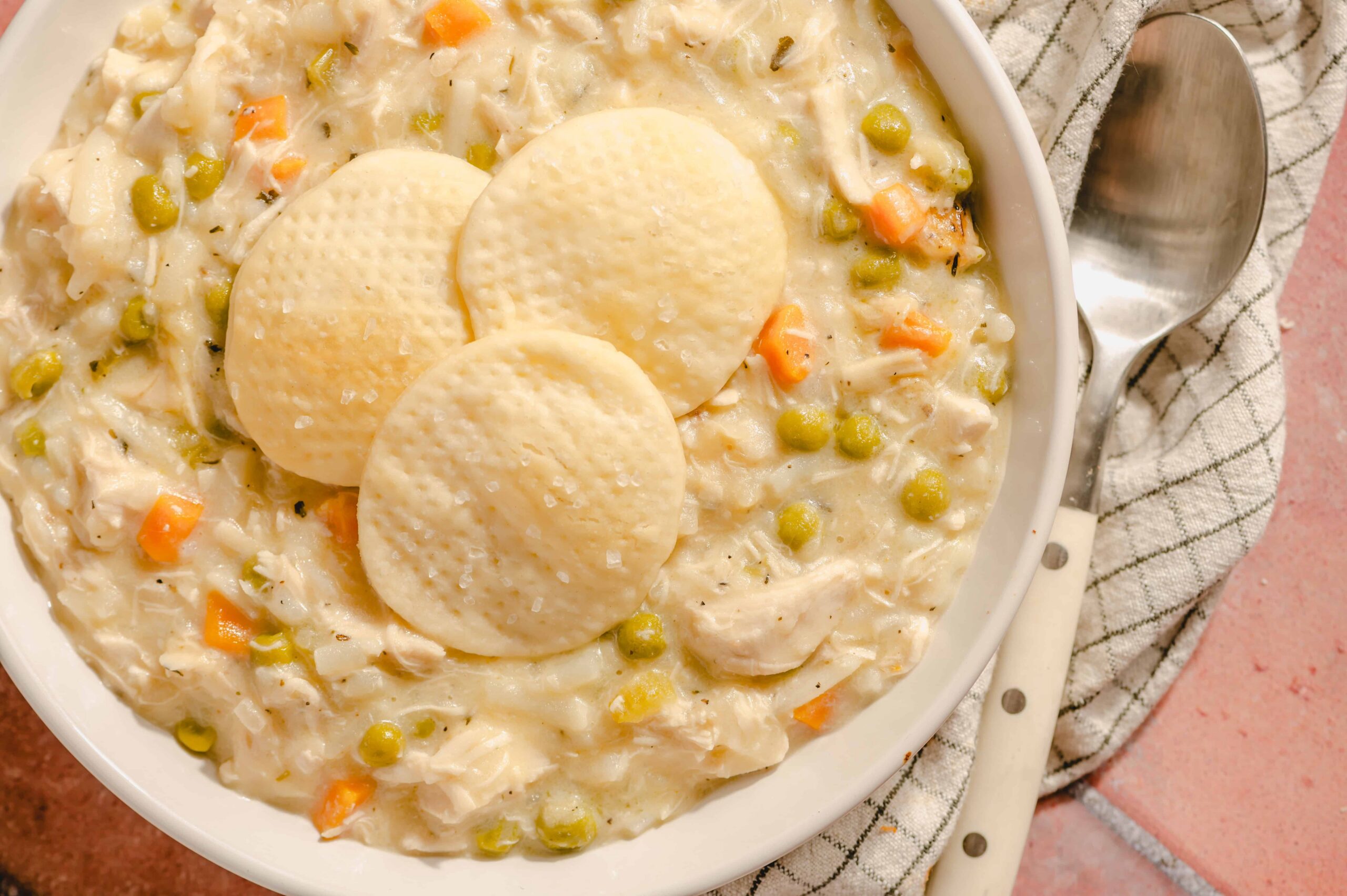 Creamy chicken and vegetable pot pie with peas, carrots, and flaky cornbread on top, served in a white bowl for a comforting homemade meal.