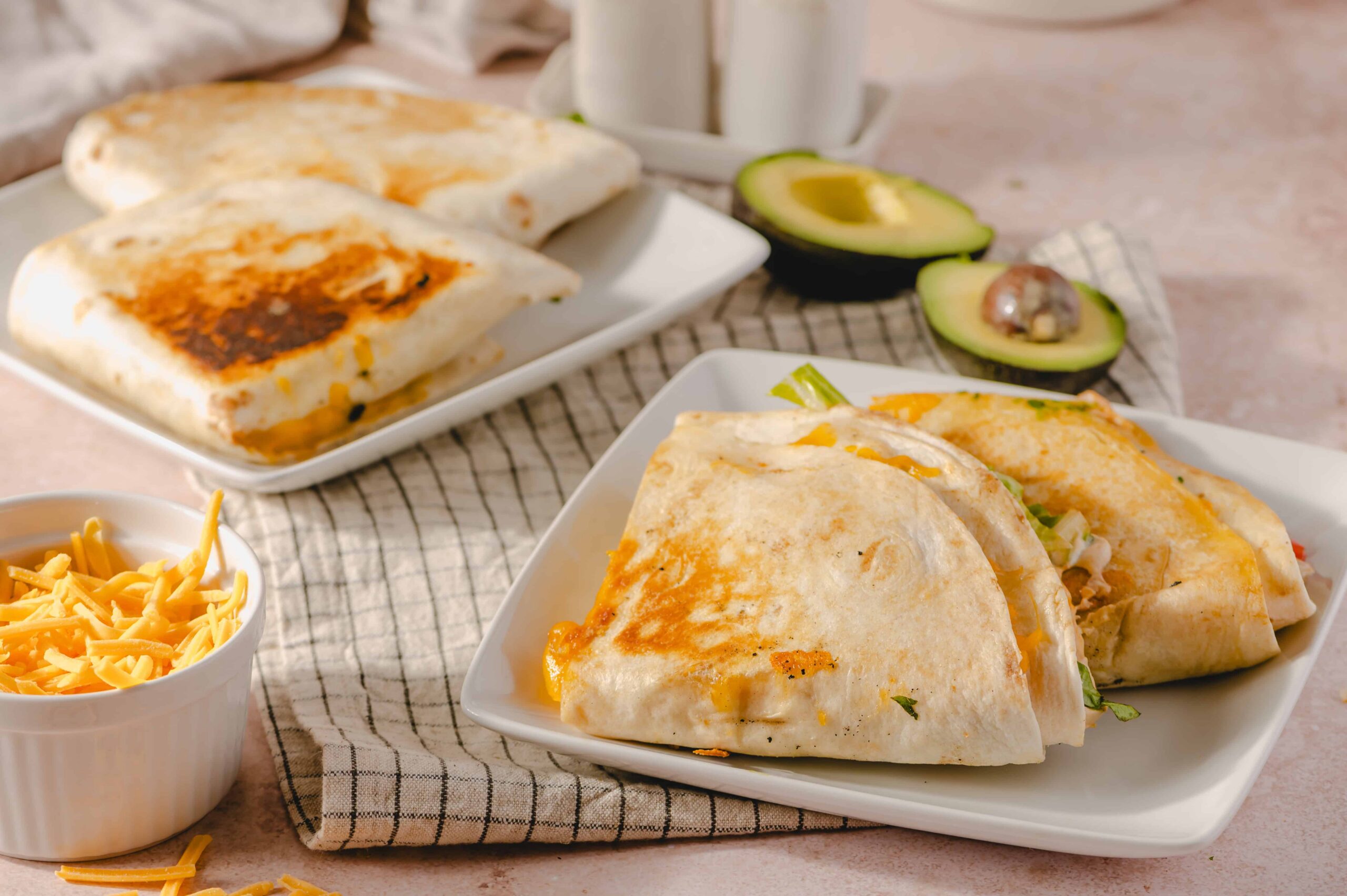 Savory breakfast burritos with melted cheese, fresh avocado, and shredded cheese on a white plate.