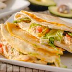 Savory chicken quesadilla with melted cheese and fresh vegetables on white plate.