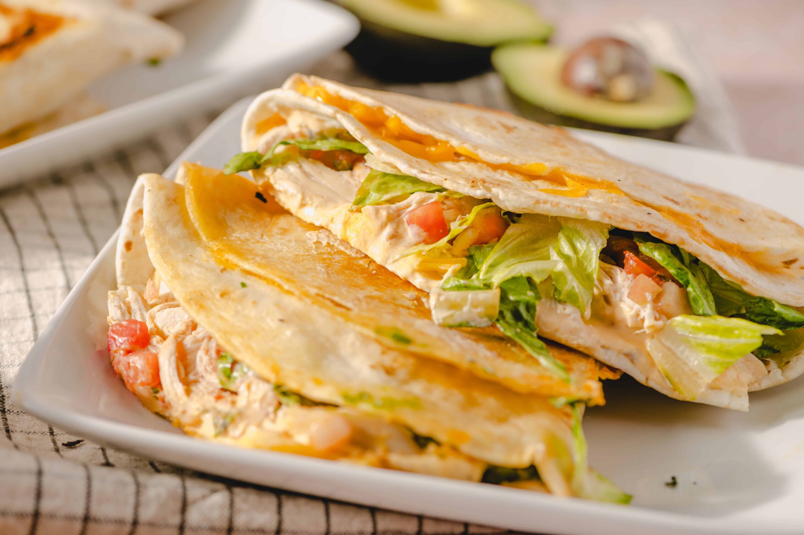 Savory chicken quesadilla with melted cheese and fresh vegetables on white plate.