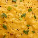Creamy mashed potatoes with melted cheese, sprinkled with black pepper and chopped green onions, showcasing a comforting and savory dish perfect for any meal.