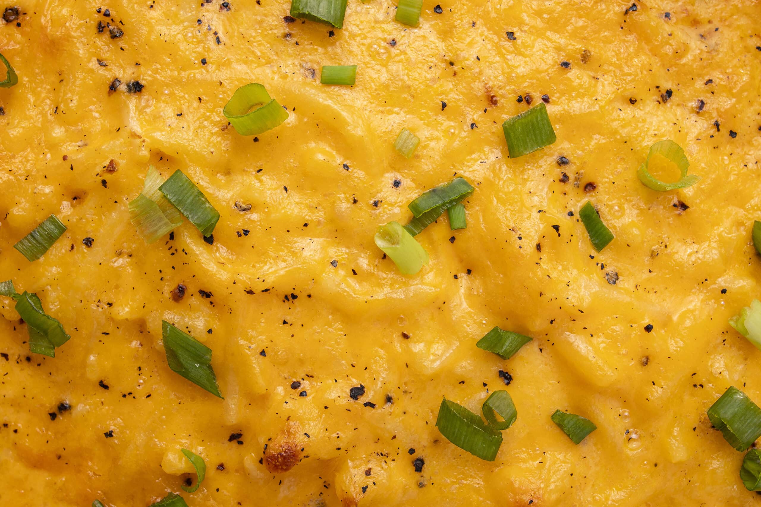 Creamy mashed potatoes with melted cheese, sprinkled with black pepper and chopped green onions, showcasing a comforting and savory dish perfect for any meal.