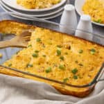Scrambled eggs with cheese garnished with chopped green onions in a glass baking dish.