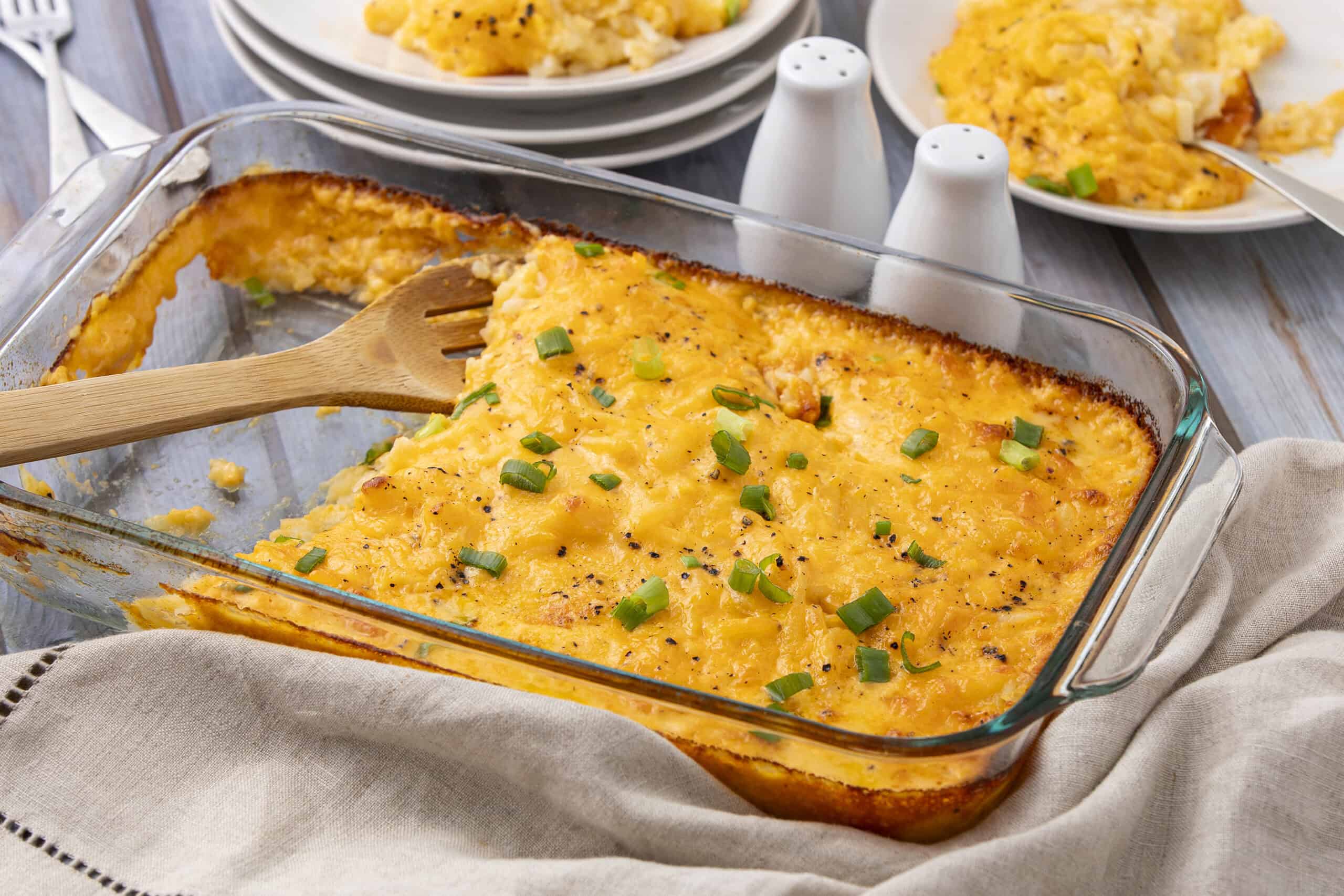 Scrambled eggs with cheese garnished with chopped green onions in a glass baking dish.