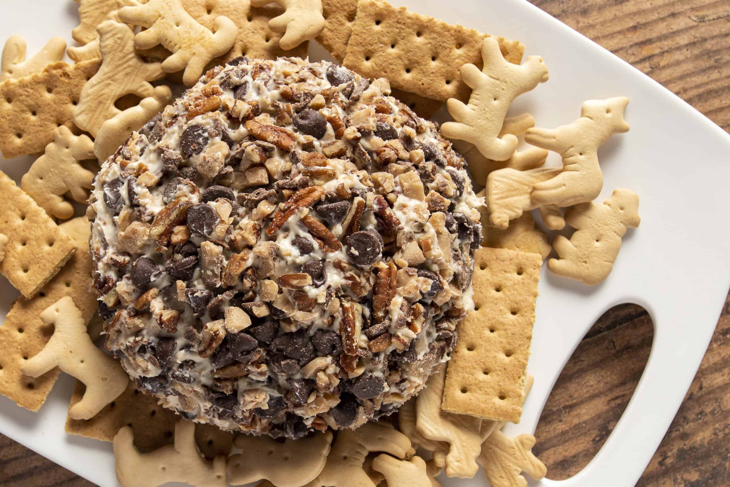 Creamy chocolate chip and chopped nut truffle coated in chocolate, served on a white platter surrounded by assorted holiday cookies and gingerbread men for festive dessert.