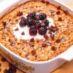 Creamy coconut baked oatmeal with blackberries and chocolate chips in a white casserole dish. Perfect healthy breakfast recipe for mornings or brunch.