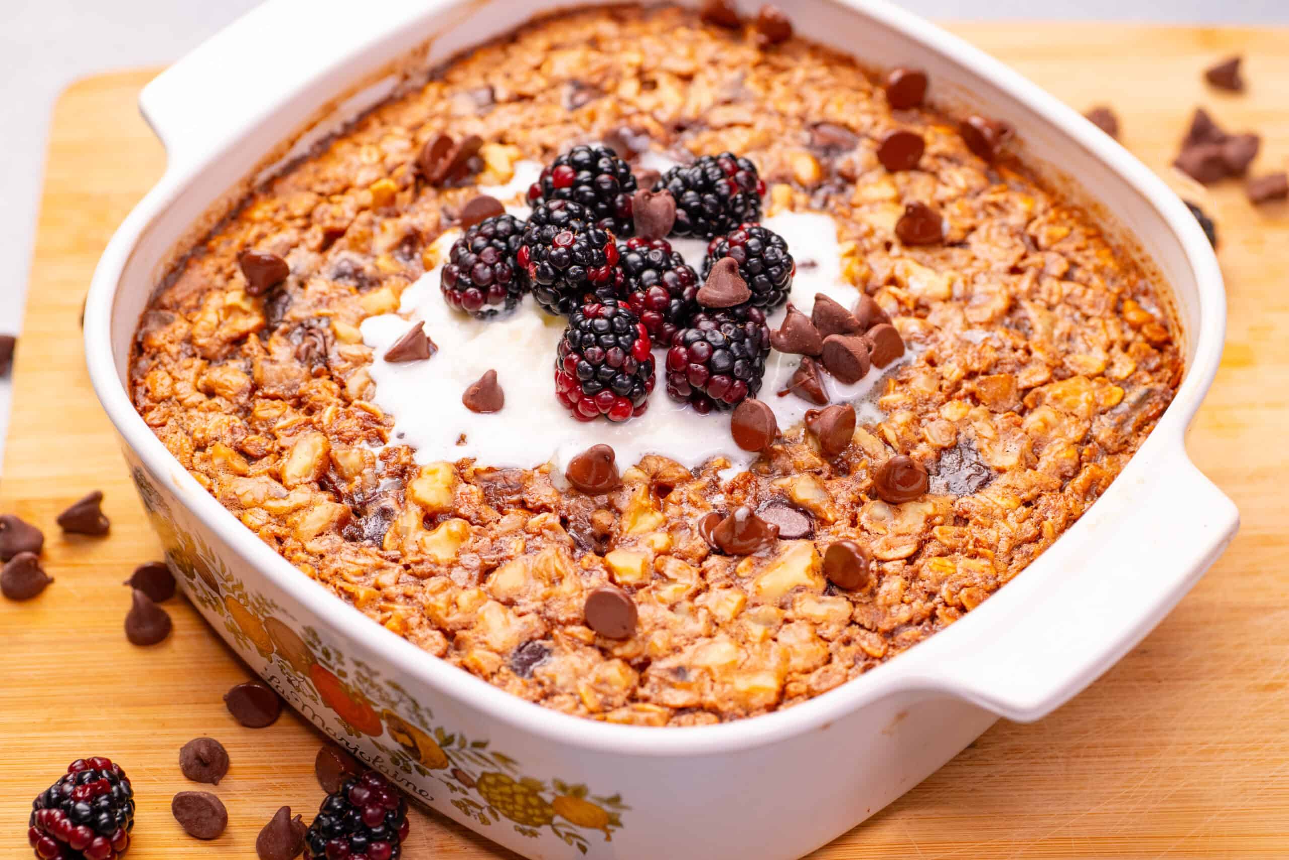Creamy coconut baked oatmeal with blackberries and chocolate chips in a white casserole dish. Perfect healthy breakfast recipe for mornings or brunch.