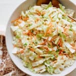 Fresh homemade coleslaw salad with shredded cabbage, carrots, green onions, and creamy dressing on a white plate, ideal for a healthy side dish or summer picnic.