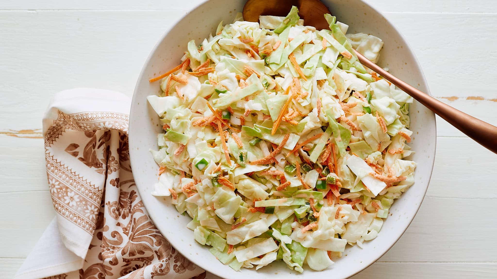 Fresh homemade coleslaw salad with shredded cabbage, carrots, green onions, and creamy dressing on a white plate, ideal for a healthy side dish or summer picnic.