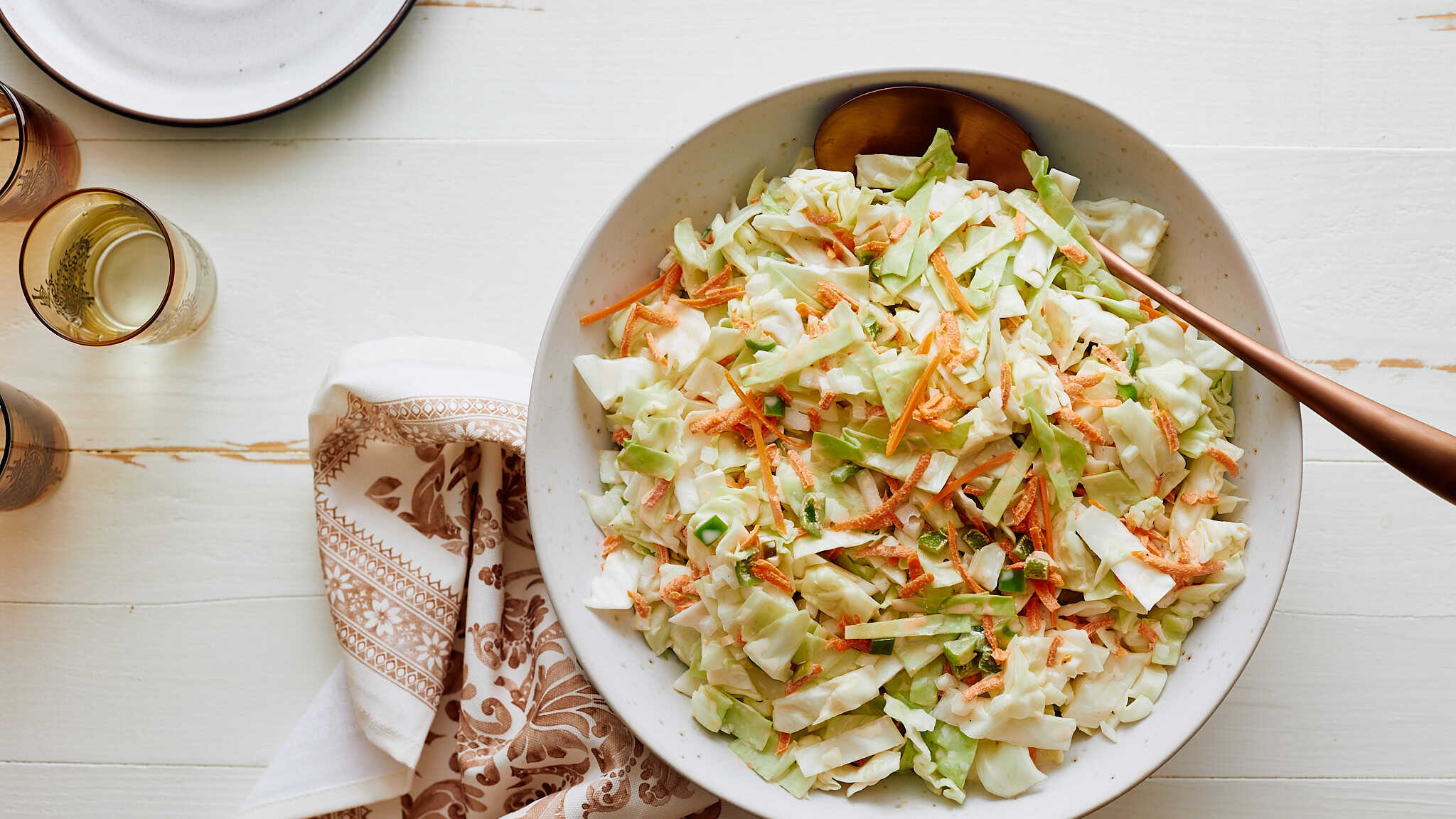 Fresh homemade coleslaw salad with shredded cabbage, carrots, and green onions in a white bowl on a light wooden table.