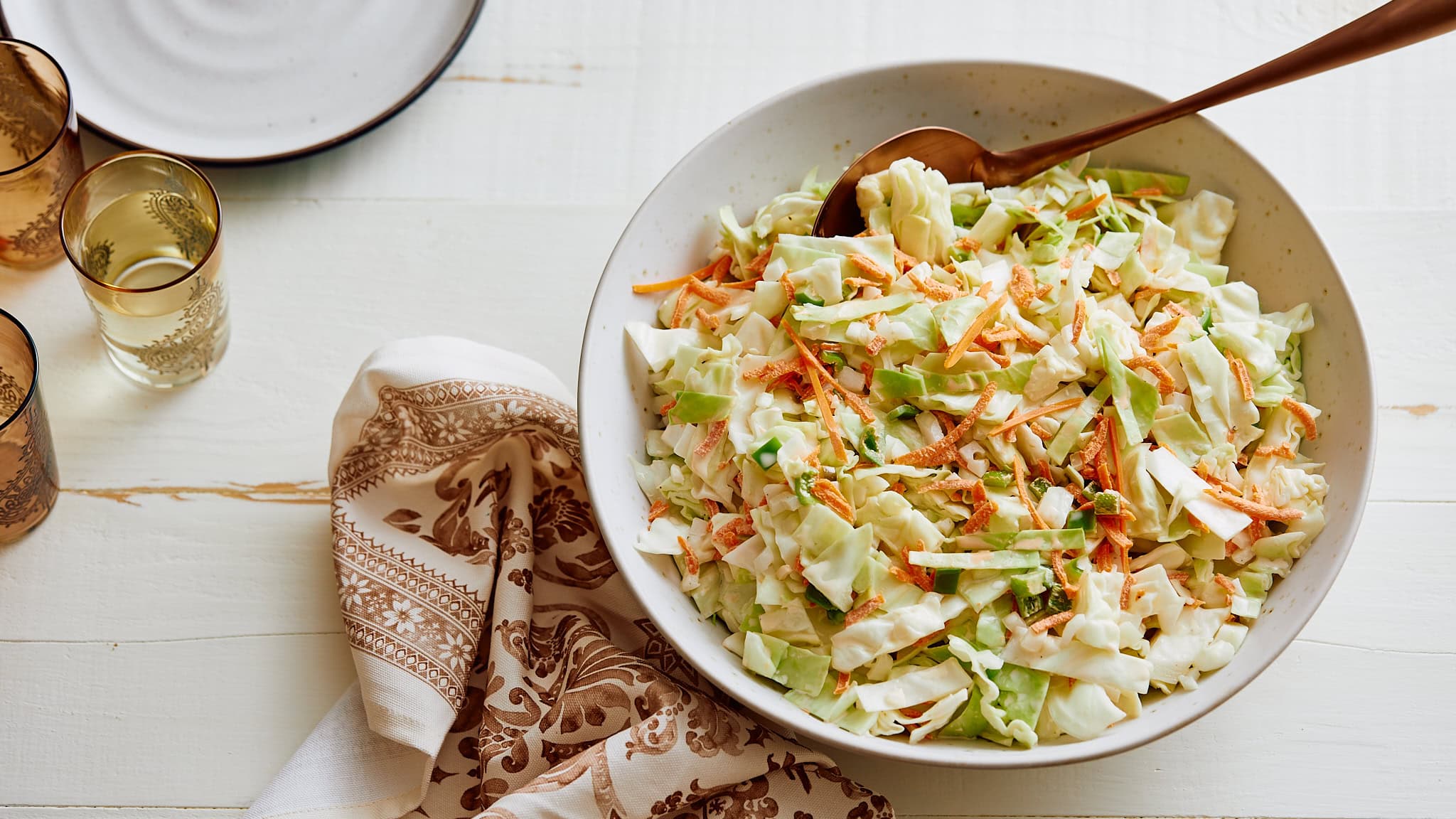 Fresh homemade coleslaw salad with cabbage, carrots, and green onions in a white ceramic bowl on a rustic white wooden table. Perfect for summer picnics and barbecues.