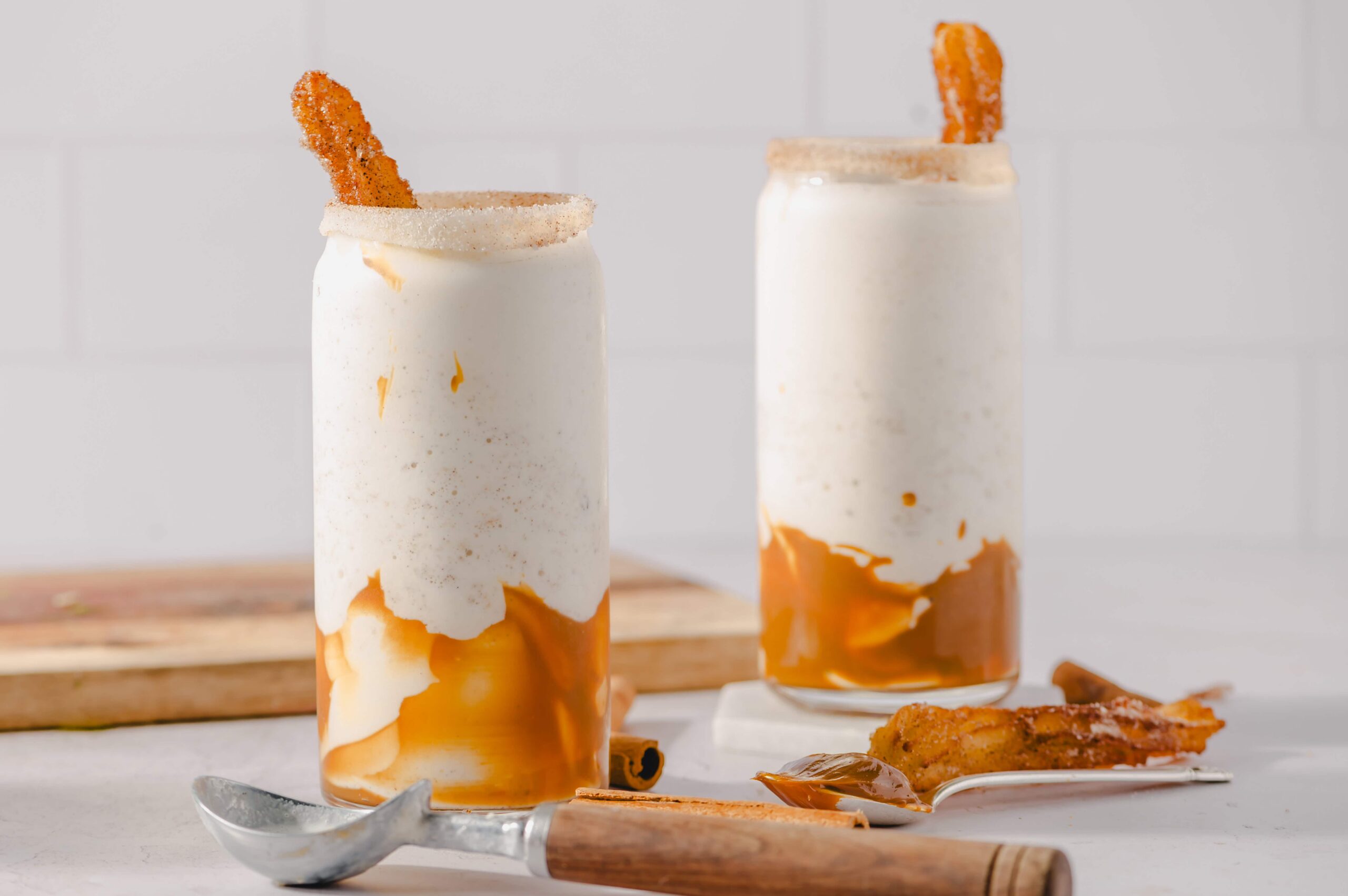 Creamy caramel milkshakes topped with cinnamon sugar churro sticks, served in tall glasses for a delicious dessert or sweet treat.