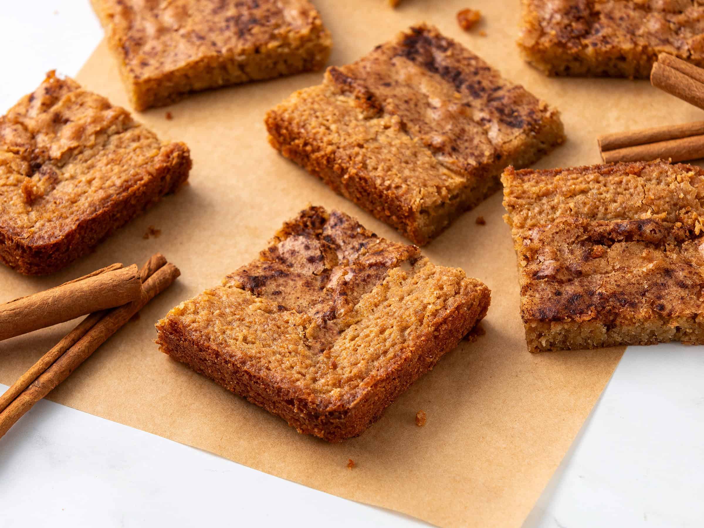 Sweet cinnamon apple crumble bars on parchment paper with cinnamon sticks, delicious, homemade dessert, cozy fall treat, easy apple dessert recipe, cinnamon-spiced crumb topping.