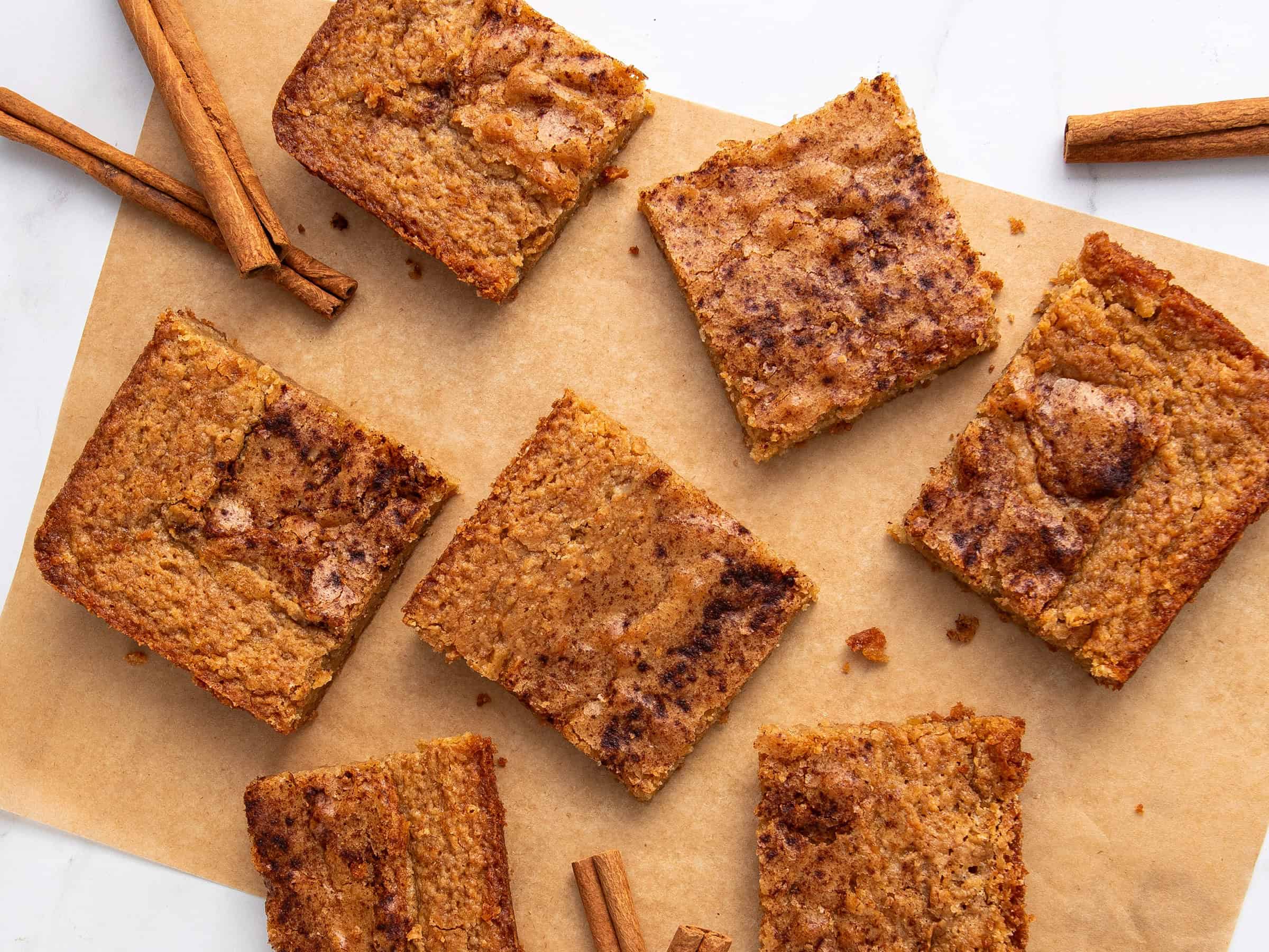 Fudgy cinnamon apple blondies with a caramelized apple topping on a parchment paper-lined surface. Perfect for fall desserts or cozy snacks with cinnamon and apple flavors.