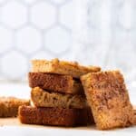 Butterscotch blondie bars stacked on a wooden cutting board with cinnamon sticks, close-up, dessert, sweet treat, no background, golden, chewy.