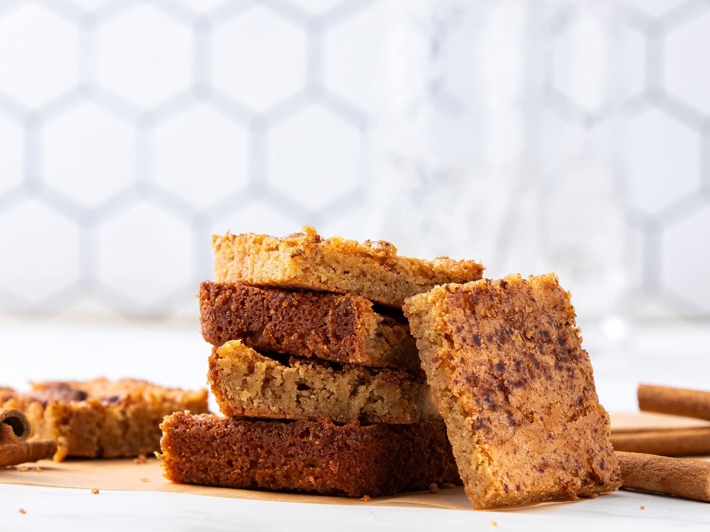Butterscotch blondie bars stacked on a wooden cutting board with cinnamon sticks, close-up, dessert, sweet treat, no background, golden, chewy.