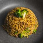 Fried rice with ground beef and broccoli served on a black plate, showcasing a savory and hearty Asian-inspired dish with vibrant green vegetables.