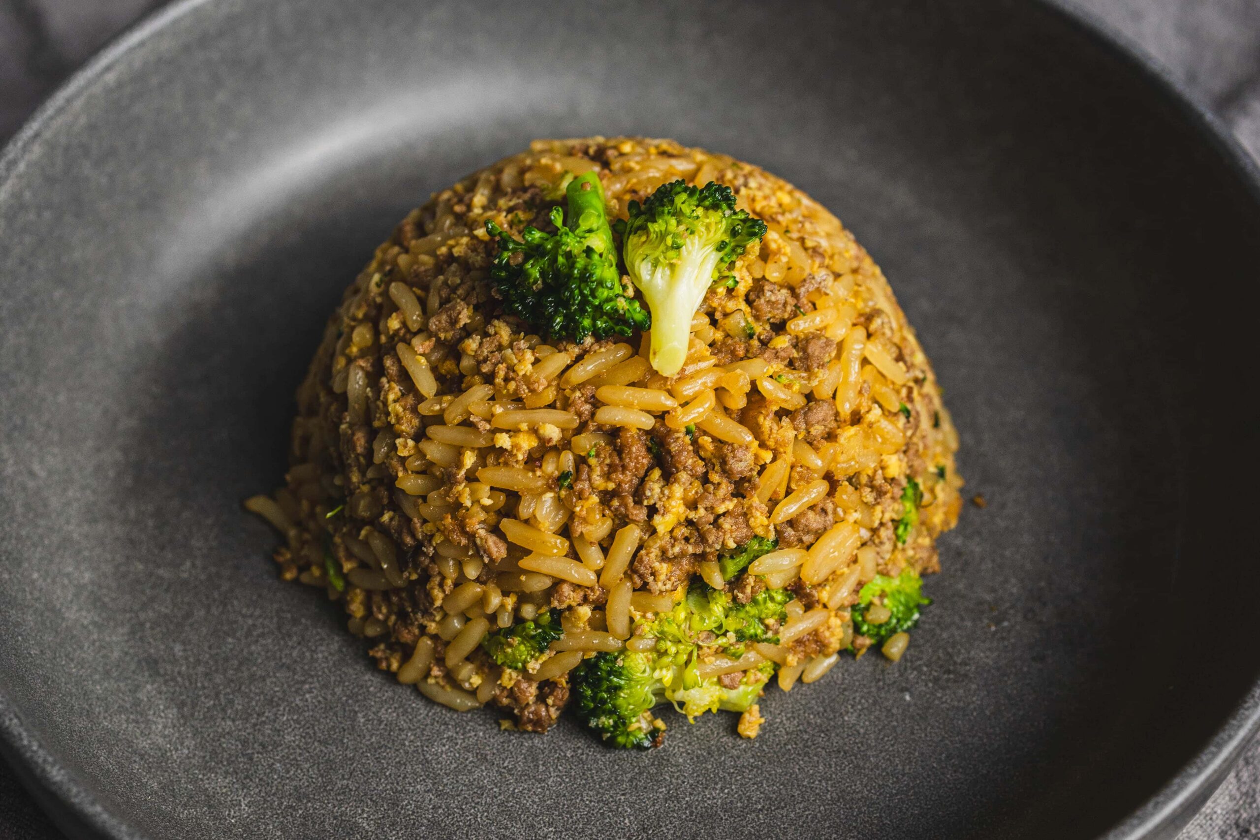 Fried rice with ground beef and broccoli served on a black plate, showcasing a savory and hearty Asian-inspired dish with vibrant green vegetables.
