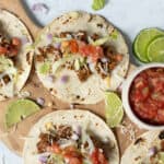 Savory beef tacos with shredded cheese lettuce and tomato in soft tortillas on wooden board with lime wedges and salsa, Mexican street food, easy taco recipe, Tex-Mex cuisine, healthy taco meal.