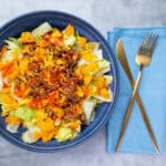 Savory taco salad with seasoned ground beef, crunchy tortilla chips, fresh lettuce, shredded cheese, and tangy salsa in a deep blue bowl.