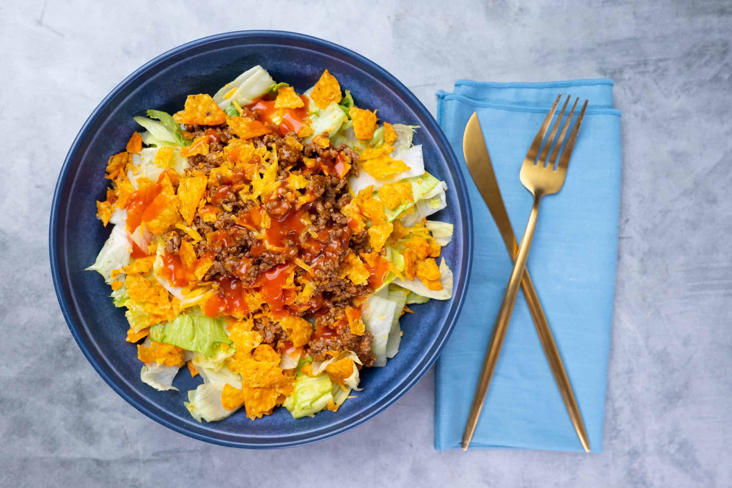 Savory taco salad with seasoned ground beef, crunchy tortilla chips, fresh lettuce, shredded cheese, and tangy salsa in a deep blue bowl.