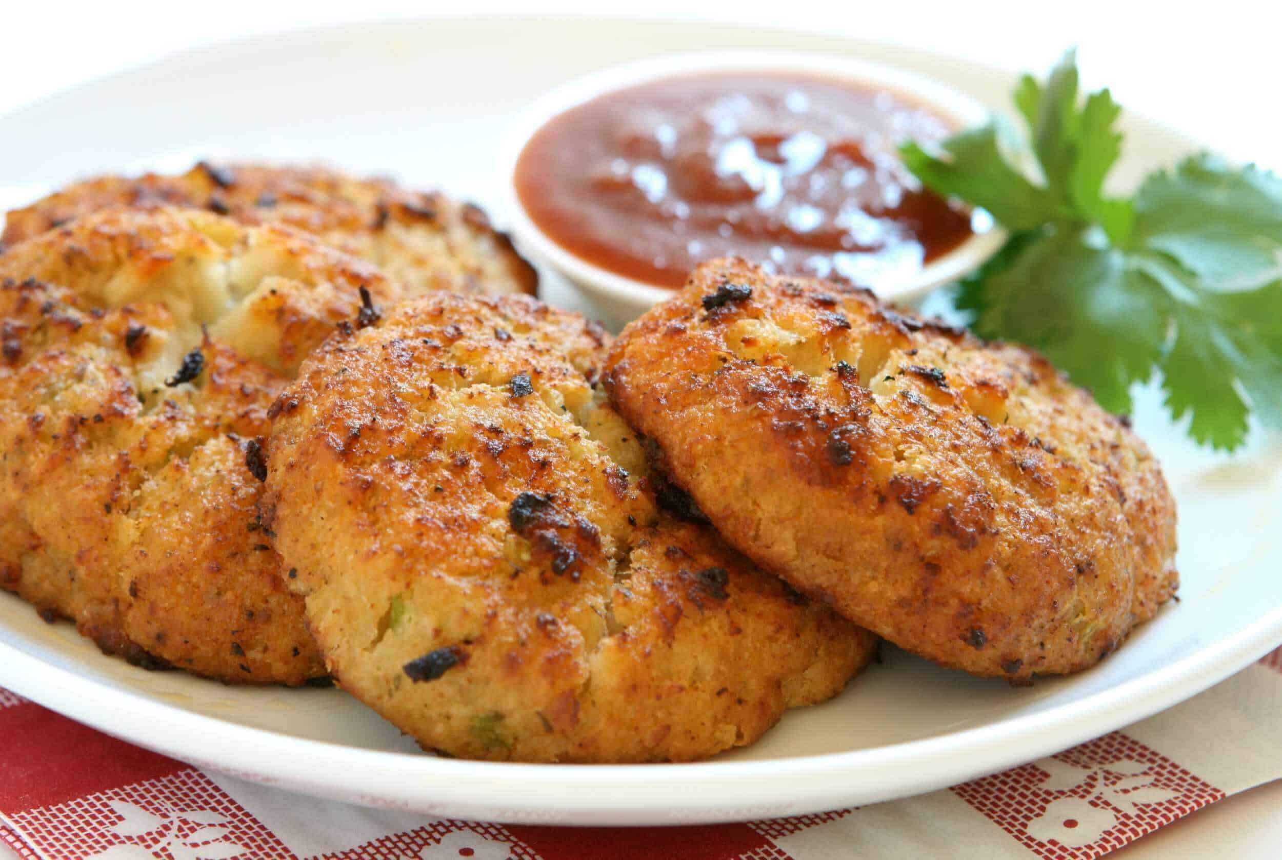Golden crispy chicken patties served with a side of spicy tomato ketchup and fresh cilantro on a white plate, perfect for appetizers or snacks.