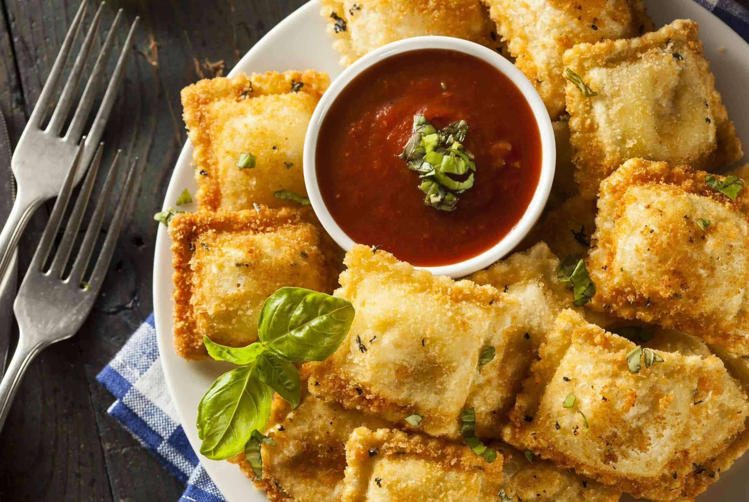 Crispy fried cheese cubes served with marinara dipping sauce, garnished with fresh basil and chopped herbs, on a white plate for a delicious appetizer or snack.