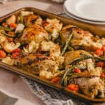 Juicy baked chicken thighs with roasted cherry tomatoes, garlic, and fresh herbs on a baking sheet for an easy dinner recipe.