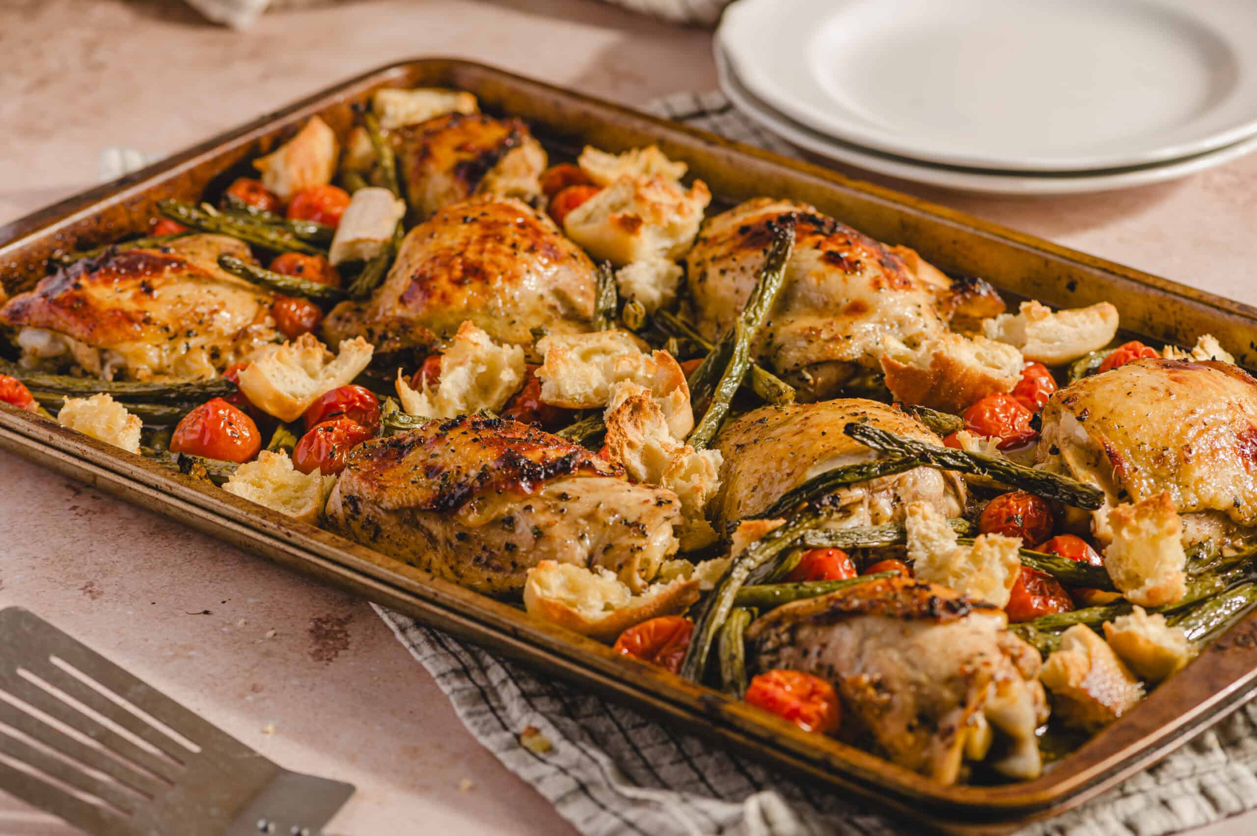 Juicy baked chicken thighs with roasted cherry tomatoes, garlic, and fresh herbs on a baking sheet for an easy dinner recipe.