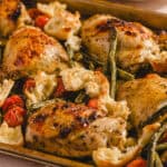 Juicy roasted chicken thighs with cherry tomatoes, roasted garlic, and fresh herbs on a baking sheet, served with warm, crispy bread. Perfect for a delicious, easy dinner or meal prep.