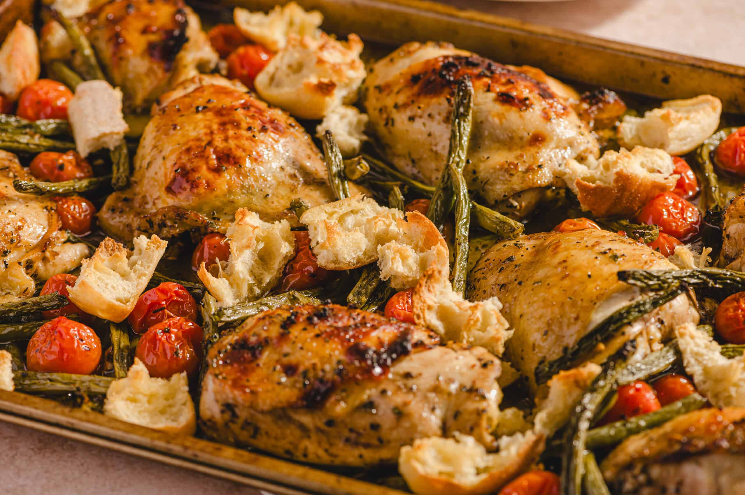 Juicy roasted chicken thighs with cherry tomatoes, roasted garlic, and fresh herbs on a baking sheet, served with warm, crispy bread. Perfect for a delicious, easy dinner or meal prep.