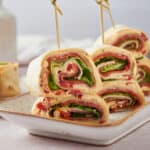 Fresh deli turkey and ham wrap roll-ups with lettuce, tomato, and cheese, sliced into bite-sized pieces for easy snacking or party finger food, served on a stylish white platter.