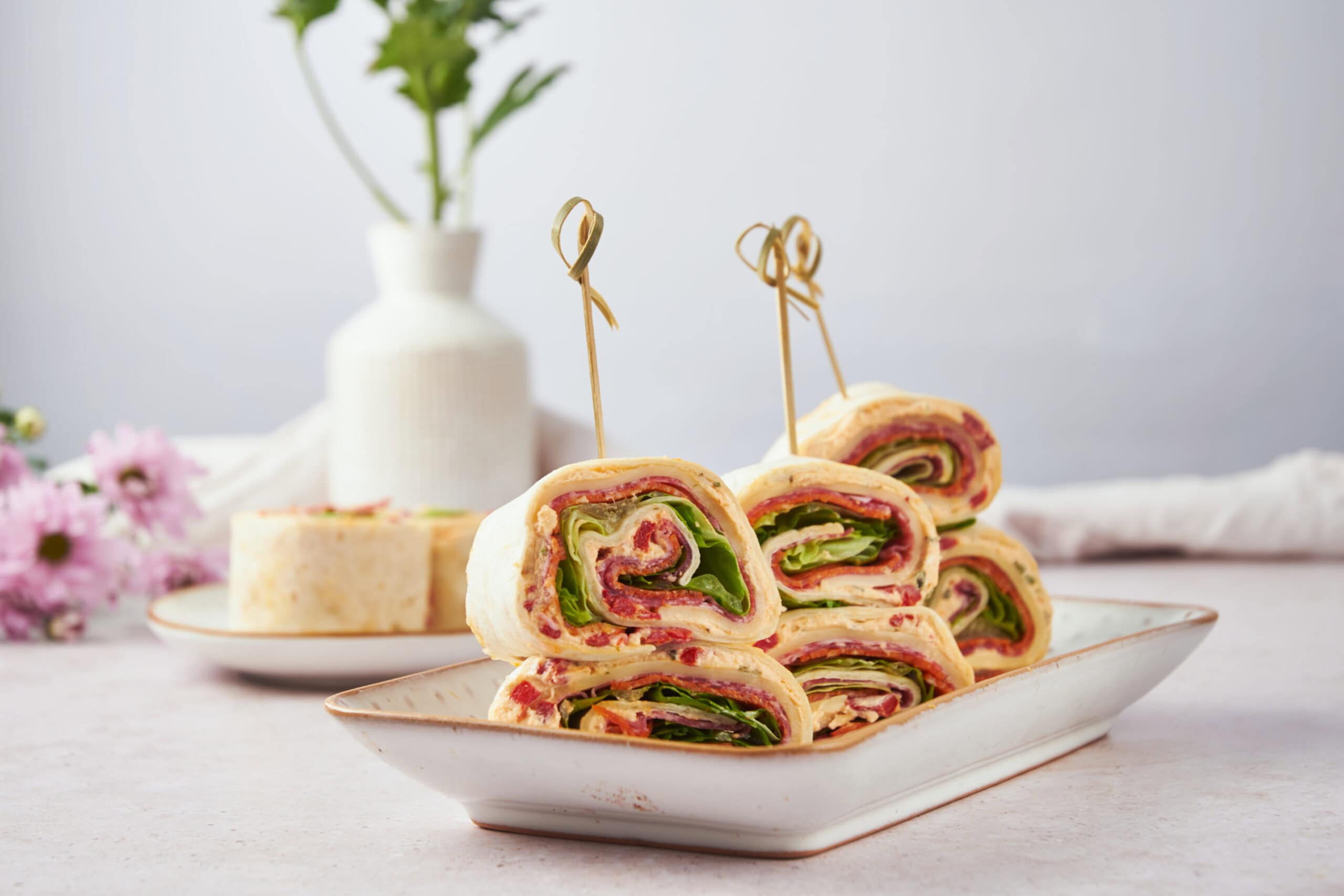 Delicious veggie and meat rolled wraps with fresh lettuce, cucumbers, and peppers, served on a white plate for a healthy snack or light meal.